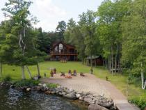 View from the lake showing docking, beach, patio fireplace, grassy yard, and large two level Red Pine Retreat.