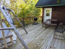 Deck area with swinging bench, picnic table, and charcoal grill.